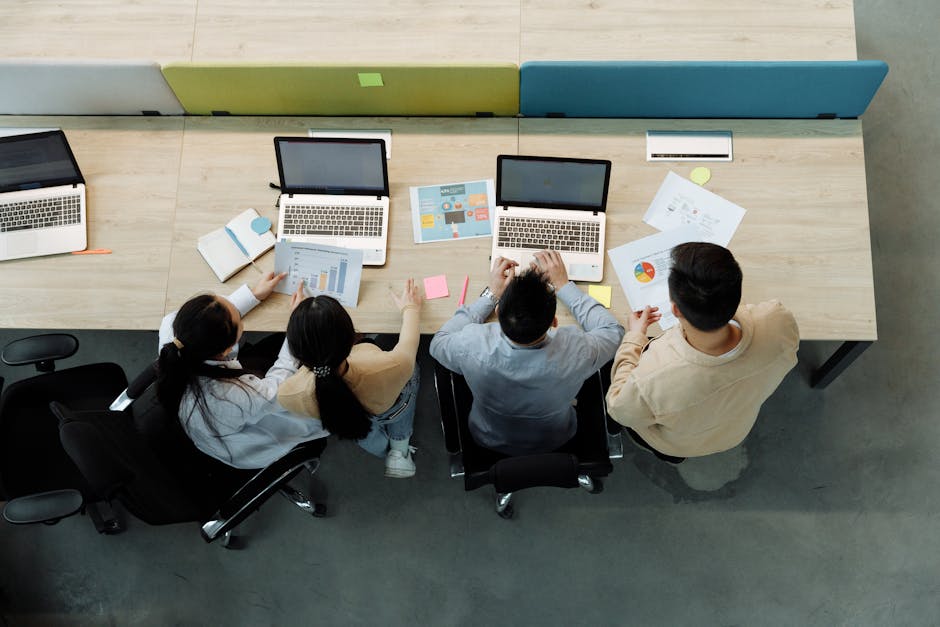 Aerial view of four colleagues working with laptops and documents at a shared desk