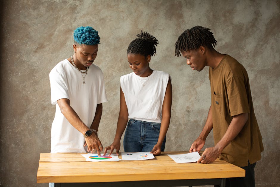 Three young adults engage in a creative project planning session, examining documents together